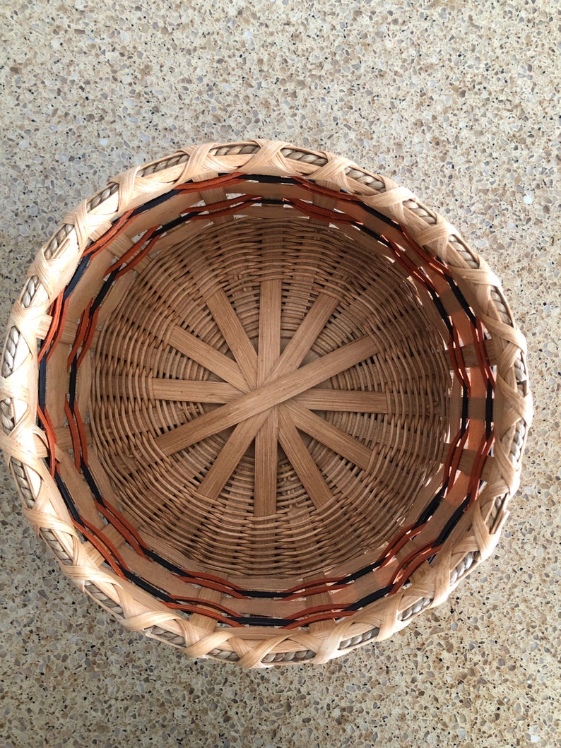 May include: A woven basket with a brown and orange rim. The basket is made of natural materials and has a circular shape.