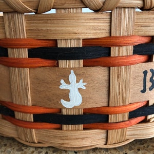 May include: A woven basket with a brown, black, and orange design. The basket has a white painted lizard on the front and the word "JB" written on the side.