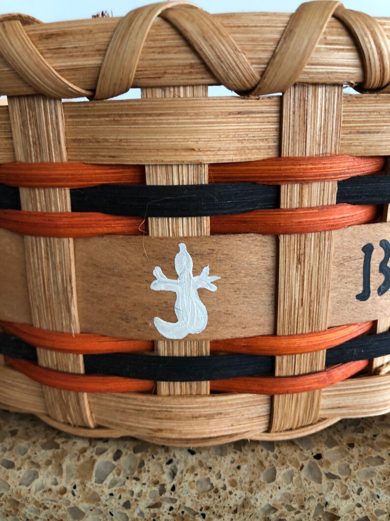 May include: A woven basket with a brown, black, and orange design. The basket has a white painted lizard on the front and the word "JB" written on the side.