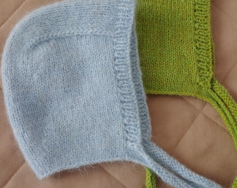 May include: Two knitted bonnets, one in a soft light blue and the other in a vibrant lime green. Each bonnet features a textured ribbed border along the face opening and long, matching knitted ties extending from the bottom corners for fastening.