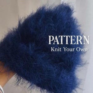 Może przedstawiać: Ciemnoniebieska, puszysta czapka z dzianiny o miękkiej, teksturowanej powierzchni. Napis "PATTERN Knit Your Own" jest nadrukowany na biało po prawej stronie czapki. Czapka ma gęsty, włóknisty wygląd z długimi, cienkimi nitkami materiału.