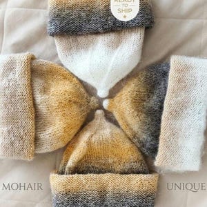 May include: Four knitted beanies arranged in a circular pattern, featuring ombre gradients of white, golden yellow, and charcoal gray. Each hat has a wide folded cuff and a pointed crown. The text READY TO SHIP and MOHAIR UNIQUE is visible.