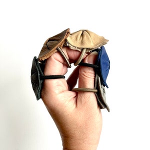 May include: Four leather hair tie holders in different colors: brown, beige, gray, and blue. The holders are made of leather and have a unique design.