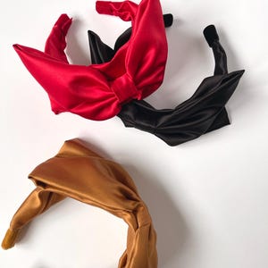 May include: Three satin headbands with knotted bows. One headband is red, one is black, and one is gold.