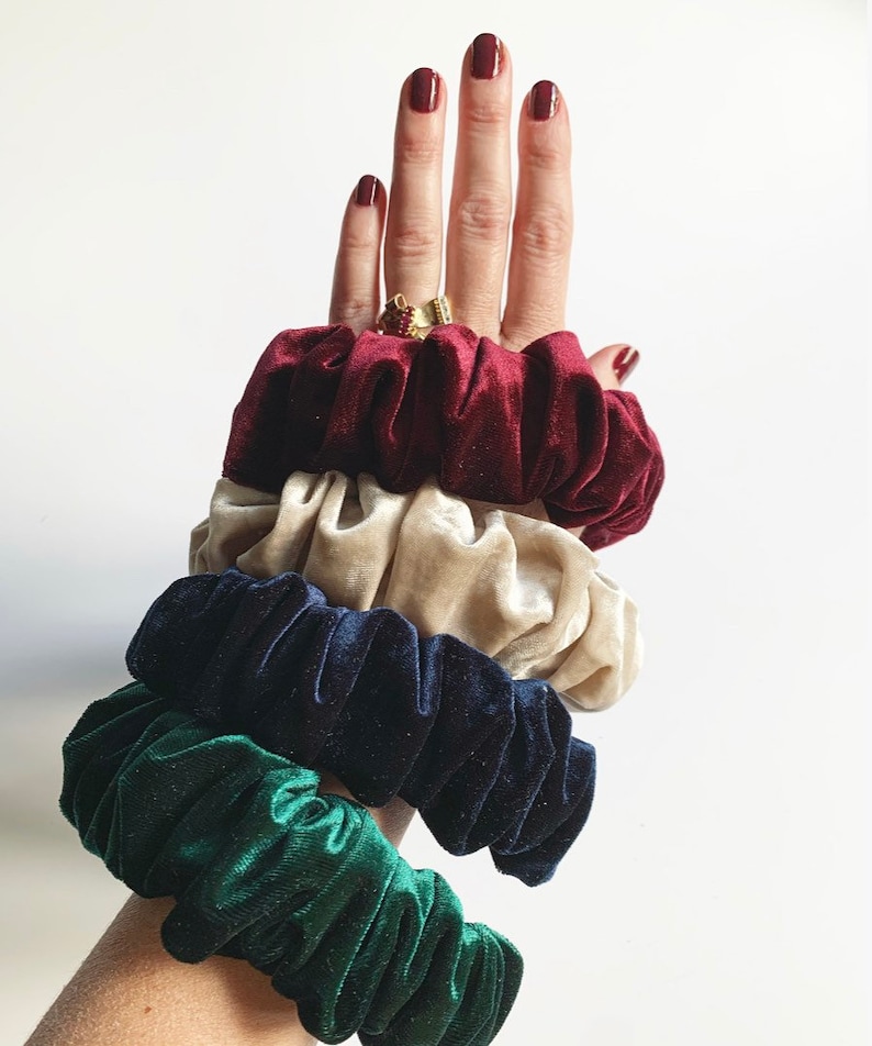 May include: A set of four scrunchies in different colors: burgundy, beige, navy blue, and green. The scrunchies are made of velvet and have a gathered, ruffled texture.