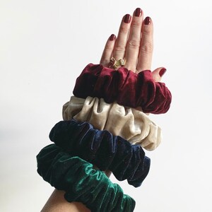 May include: Set of four scrunchies in different colors: burgundy, cream, navy blue, and forest green. The scrunchies are made of soft velvet and are stacked on top of each other.