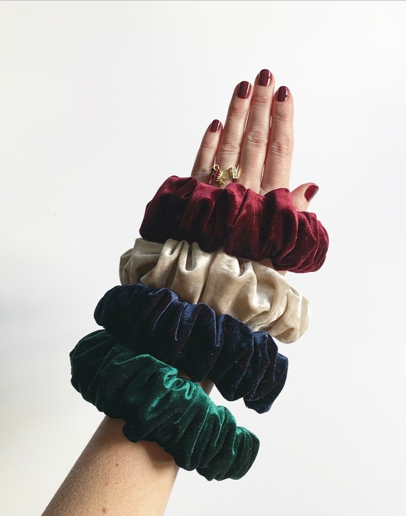 May include: Set of four scrunchies in different colors: burgundy, cream, navy blue, and forest green. The scrunchies are made of soft velvet and are stacked on top of each other.
