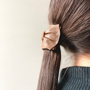 May include: A brown leather hair tie in the shape of a bow, tied around a ponytail of long brown hair.
