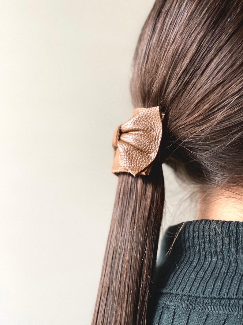 May include: A brown leather hair tie in the shape of a bow, tied around a ponytail of long brown hair.