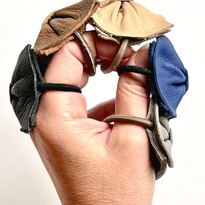 May include: Five leather fingertip protectors in different colors: black, brown, beige, gray, and blue. Each protector is attached to a hair elastic.