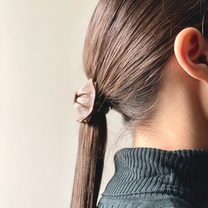 May include: A person with long brown hair tied back with a brown leather hair tie. The person is wearing a dark green turtleneck sweater.