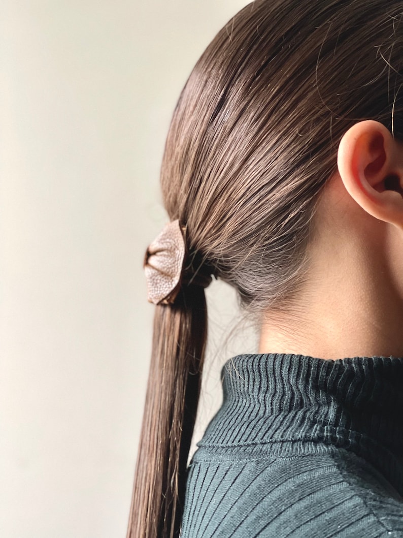 May include: A person with long brown hair tied back with a brown leather hair tie. The person is wearing a dark green turtleneck sweater.