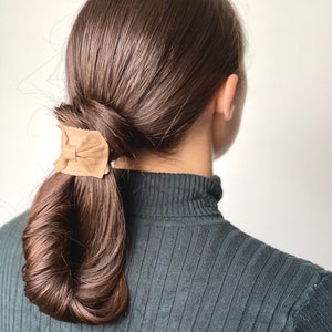 May include: A woman with long brown hair tied back in a low ponytail with a brown leather hair tie.