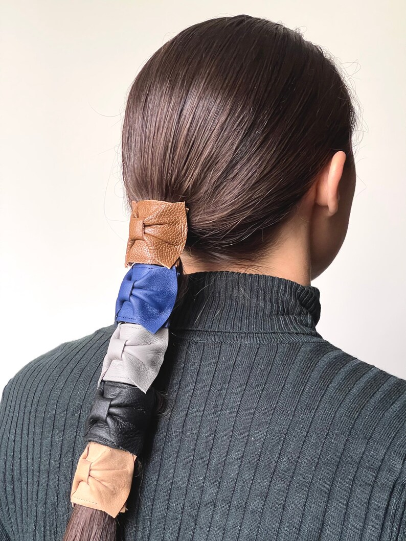 May include: A ponytail holder with four leather bows in brown, blue, gray, and beige.