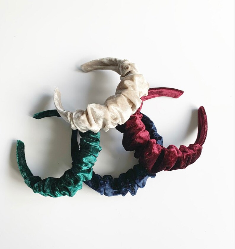 May include: Four velvet headbands in different colors: cream, dark green, navy blue, and burgundy. The headbands are all gathered and have a simple, elegant design.