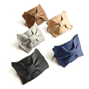 May include: Five leather bracelets with bow accents in different colors: brown, gray, beige, blue, and black.
