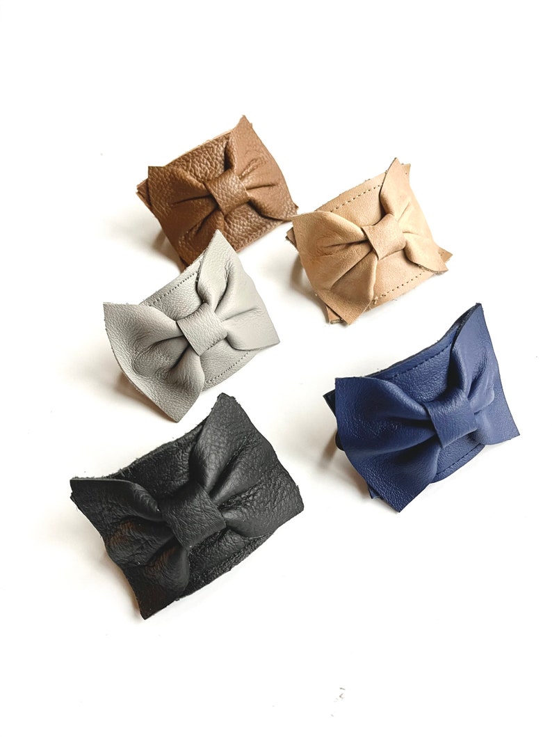 May include: Five leather bracelets with bow accents in different colors: brown, gray, beige, blue, and black.