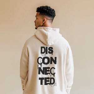 Peut inclure: Un sweat à capuche beige avec un imprimé graphique noir qui dit "DISCONNECTED" au dos.