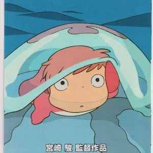 May include: A promotional poster for the animated film "Ponyo on the Cliff by the Sea." The image features a cartoon character with red hair and a blue hooded garment. The background shows a seascape with boats and the film's title in Japanese and English.