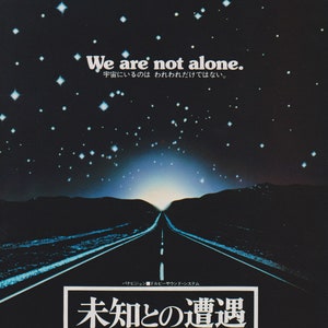 May include: A movie poster for the film Close Encounters of the Third Kind. The poster features a long, straight road leading to a bright light in the distance. The sky is filled with stars. The text on the poster reads "We are not alone.  宇宙にいるのはわれわれだけではない。" and "未知との遭遇 Close Encounters of the Third Kind".