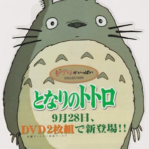 May include: A die-cut sticker featuring the character Totoro, a large grey creature with a beige belly and pointed ears. The image includes Japanese text, the word COLLECTION, and the phrase 9月28日、DVD2枚組で新登場!! printed in black, green, and orange.