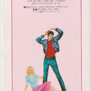 Può includere: Un poster cinematografico vintage del musical "Grease" con John Travolta e Olivia Newton-John. Il poster ha uno sfondo rosa con il titolo del film in grandi lettere rosse e il titolo giapponese sottostante. Gli attori sono raffigurati con abiti degli anni '50.