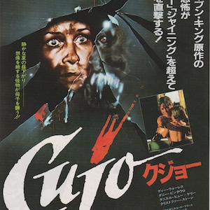 Puede incluir: Un póster de película de terror para la película "Cujo" basada en la novela de Stephen King. El póster presenta a una mujer que parece aterrorizada mirando a través de una ventana rota con el rostro de un perro amenazante reflejado en el vidrio. El título "Cujo" está escrito en blanco con un efecto de salpicadura roja.