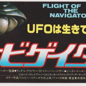 Può includere: Un poster del film Flight of the Navigator, che presenta un'astronave con un grande oblò a forma di occhio. Il poster è in giapponese e inglese e include il testo "UFO is alive." e "Navigator".