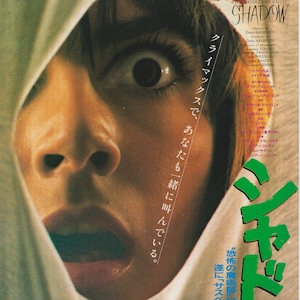 May include: A movie poster for the film "Shadow" directed by Dario Argento. The poster features a close-up of a woman's face with a terrified expression. The woman is partially covered by a white sheet. The poster also features the title of the film in large green letters and the text "クライマックスで、あなたも一緒に叫んでいる。" in Japanese.