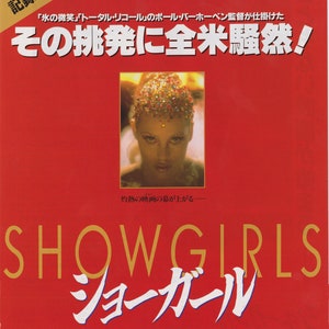 May include: A red movie poster with the title "Showgirls" in gold letters. The poster features a woman with glitter on her hair and a serious expression. The text on the poster reads "The challenge to the whole country!" and "The curtain of the burning movie rises."