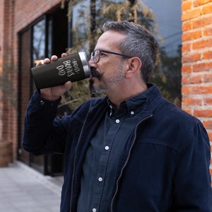 May include: A black stainless steel travel mug with a white inscription that reads "Bonus Dad".