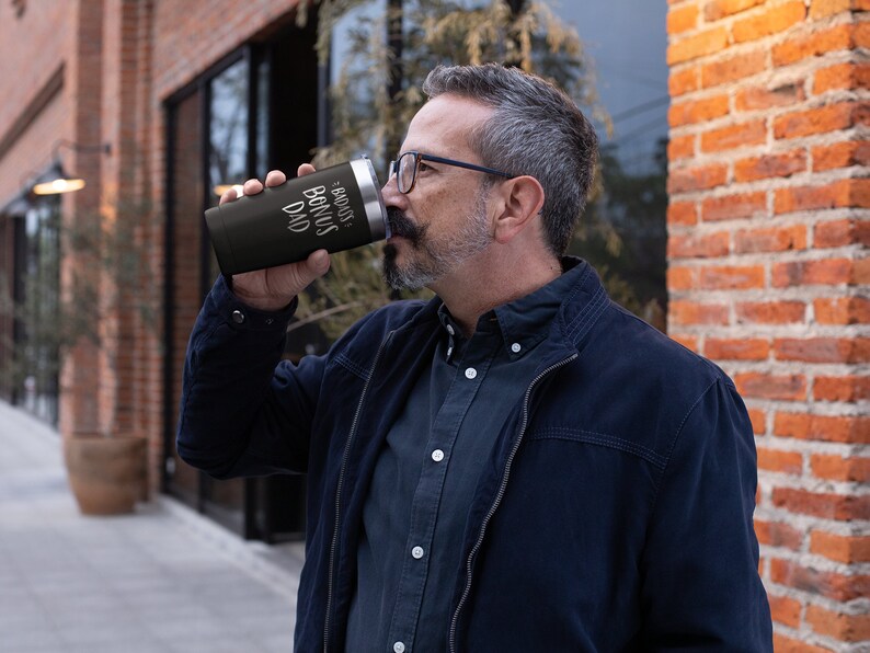 May include: A black stainless steel travel mug with a white inscription that reads "Bonus Dad".