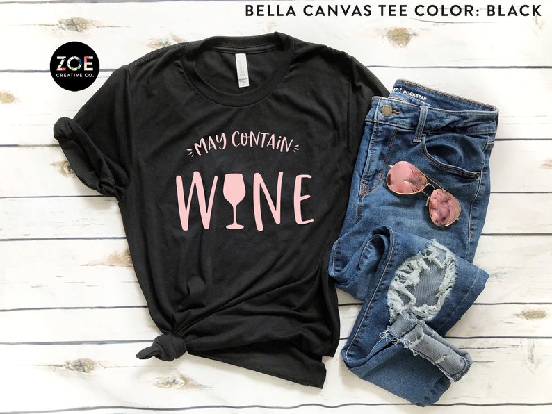 Może przedstawiać: Czarny T-shirt Bella Canvas z napisem "May Contain Wine" w r&oacute;żowych literach z grafiką r&oacute;żowego kieliszka do wina.