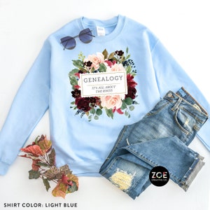 Peut inclure: Sweat-shirt bleu clair avec un motif floral et le texte "Genealogie C'est tout ce qui compte les racines".