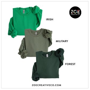 May include: Three long-sleeved sweatshirts in shades of green: Irish, Military, and Forest. The sweatshirts are neatly folded, with the sleeves bunched up. The brand name "ZOE CREATIVE CO." is displayed on the bottom and the logo is in the upper right corner.