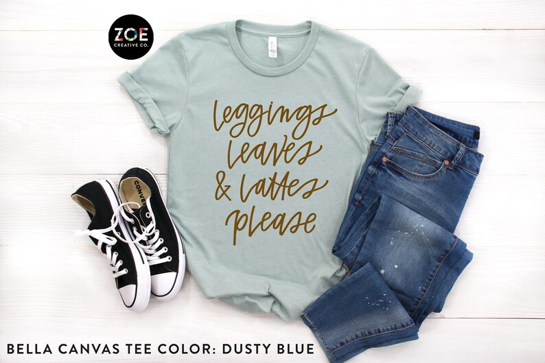 May include: A dusty blue Bella Canvas t-shirt with the text "leggings leaves & lattes please" in brown lettering.