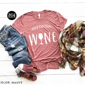 K&ouml;nnte beinhalten: Mauvefarbenes T-Shirt mit dem Text "May Contain Wine" und einer wei&szlig;en Weinglasgrafik.