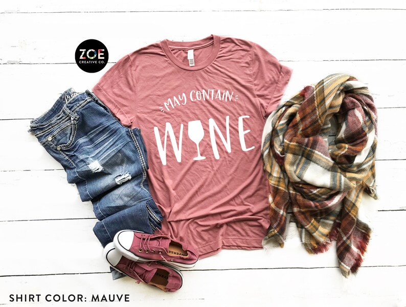 K&ouml;nnte beinhalten: Mauvefarbenes T-Shirt mit dem Text "May Contain Wine" und einer wei&szlig;en Weinglasgrafik.