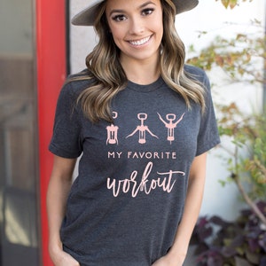 May include: A dark grey t-shirt with a pink graphic of three wine openers and the text "My Favorite Workout".