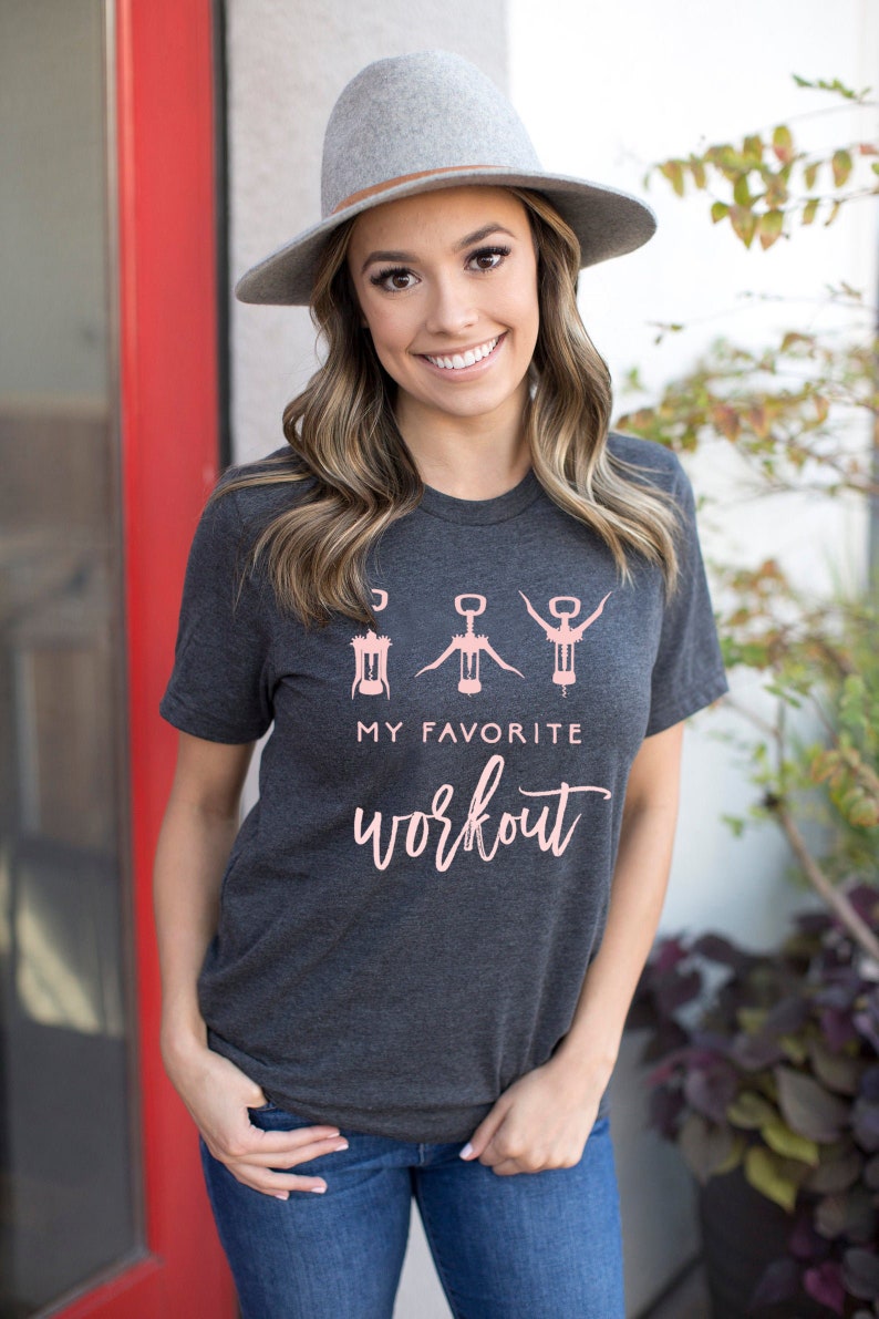 May include: A dark grey t-shirt with a pink graphic of three wine openers and the text "My Favorite Workout".