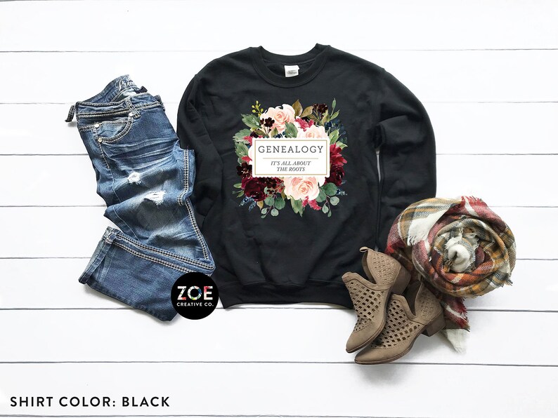 Peut inclure: Sweat-shirt noir avec un motif floral et le texte "Genealogie C'est tout ce qui compte les racines".