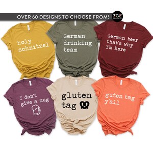Op de afbeelding: Zes verschillende T-shirts met Duitse tekst en ontwerpen. De shirts zijn in verschillende kleuren, waaronder mosterdgeel, olijfgroen, bordeauxrood, heidepaars, beige en oranje. De tekst op de shirts is: "holy schnitzel", "German drinking team", "German beer that's why I'm here", "I don't give a mug", "gluten tag" en "guten tag y'all".