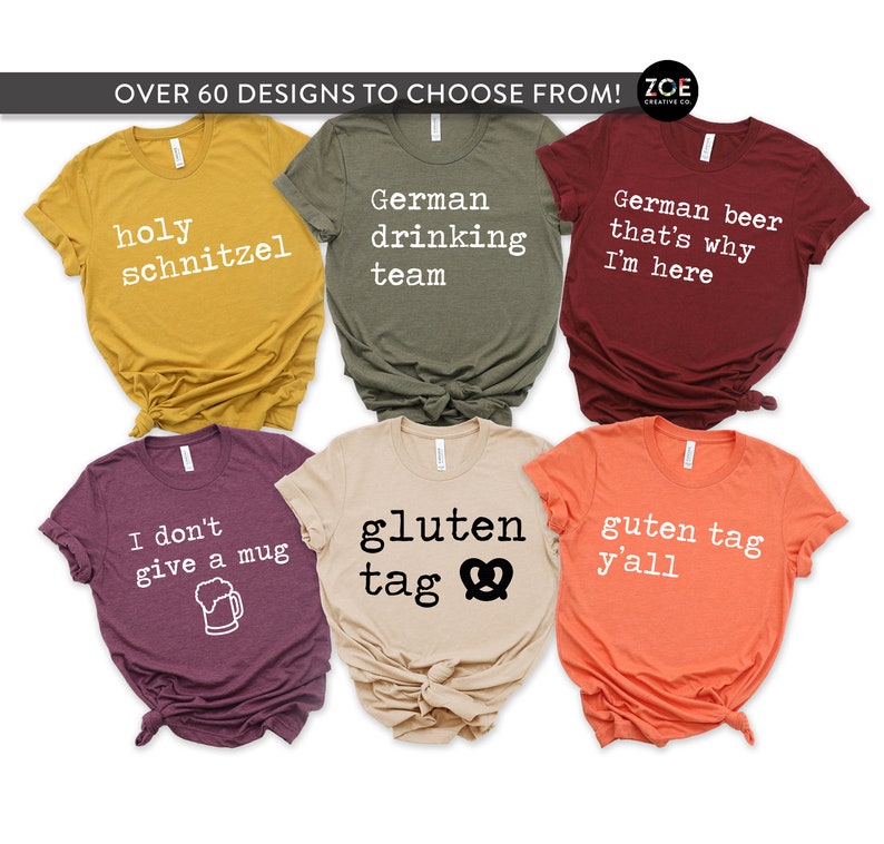 Op de afbeelding: Zes verschillende T-shirts met Duitse tekst en ontwerpen. De shirts zijn in verschillende kleuren, waaronder mosterdgeel, olijfgroen, bordeauxrood, heidepaars, beige en oranje. De tekst op de shirts is: "holy schnitzel", "German drinking team", "German beer that's why I'm here", "I don't give a mug", "gluten tag" en "guten tag y'all".