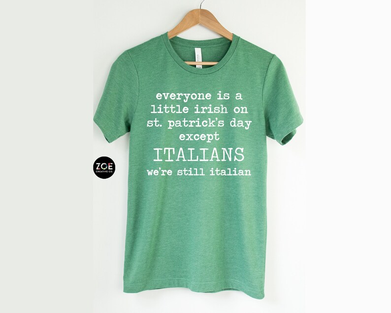 May include: Green t-shirt with white text: "everyone is a little irish on st. patrick's day except ITALIANS we're still italian." The shirt is hanging on a wooden hanger. The brand logo "ZOE CREATIVE CO." is on the bottom left.