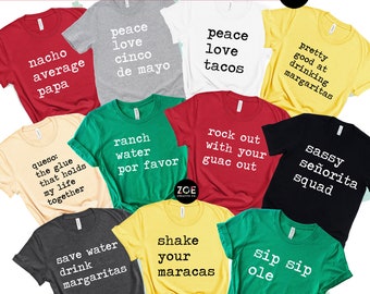 May include: A collection of 10 t-shirts with various designs and text, including "nacho average papa", "peace love tacos", "ranch water por favor", "rock out with your guac out", "sassy señorita squad", "sip sip ole", "save water drink margaritas", "shake your maracas", "queso: the glue that holds my life together", and "pretty good at drinking margaritas".