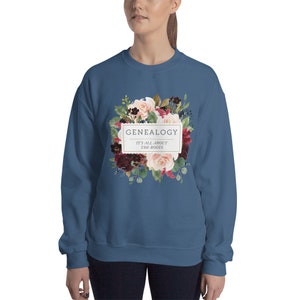 Peut inclure: Un sweat-shirt bleu fonc&eacute; avec un motif floral et le texte "GENEALOGY IT'S ALL ABOUT THE ROOTS" dans un rectangle blanc.