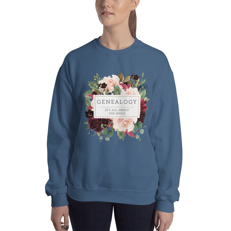 Peut inclure: Un sweat-shirt bleu fonc&eacute; avec un motif floral et le texte "GENEALOGY IT'S ALL ABOUT THE ROOTS" dans un rectangle blanc.