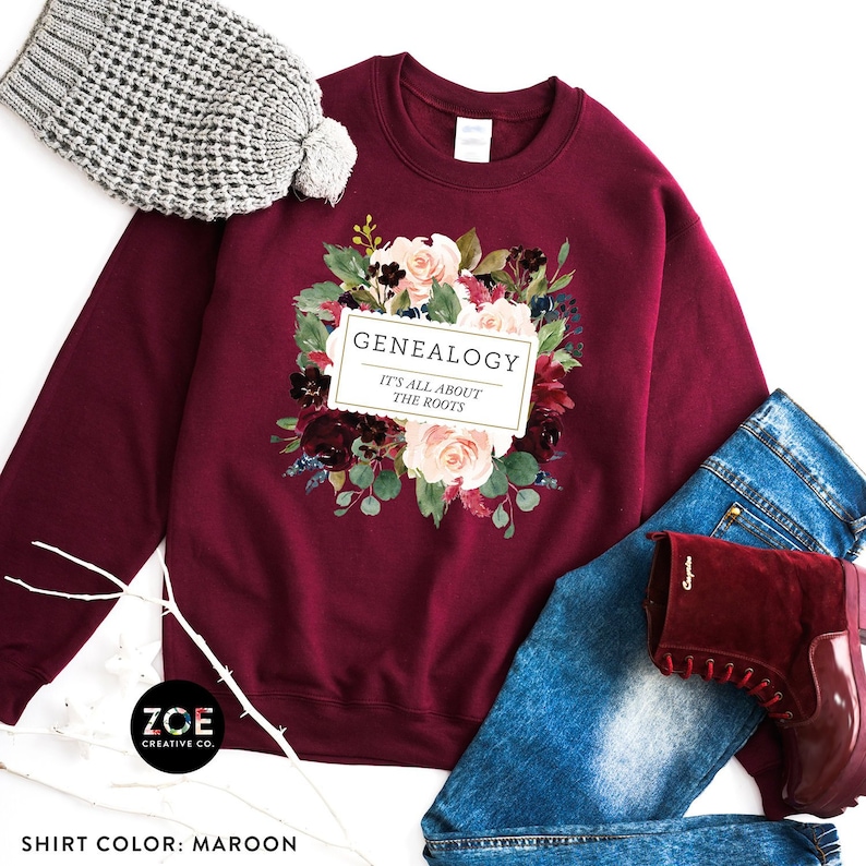 Peut inclure: Sweat-shirt bordeaux avec un motif floral et le texte "GENEALOGY IT'S ALL ABOUT THE ROOTS".