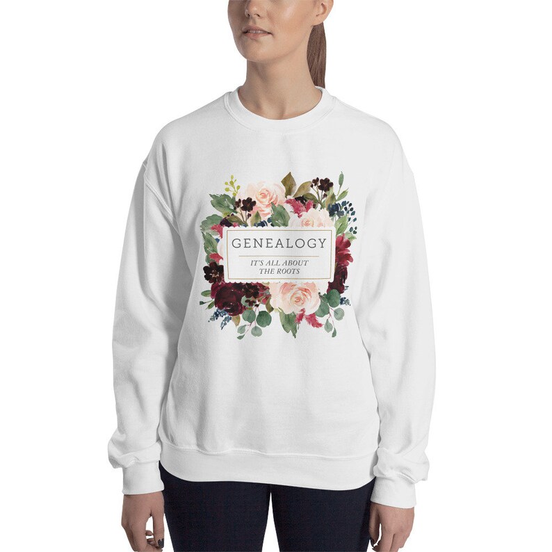 Peut inclure: Sweat-shirt blanc avec un motif floral et le texte "GENEALOGY IT'S ALL ABOUT THE ROOTS" dans un cadre dor&eacute;.