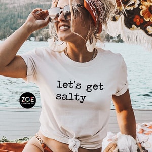 May include: White t-shirt with the text "let's get salty" printed in black. The shirt is being worn by a person with a red bandana and sunglasses.